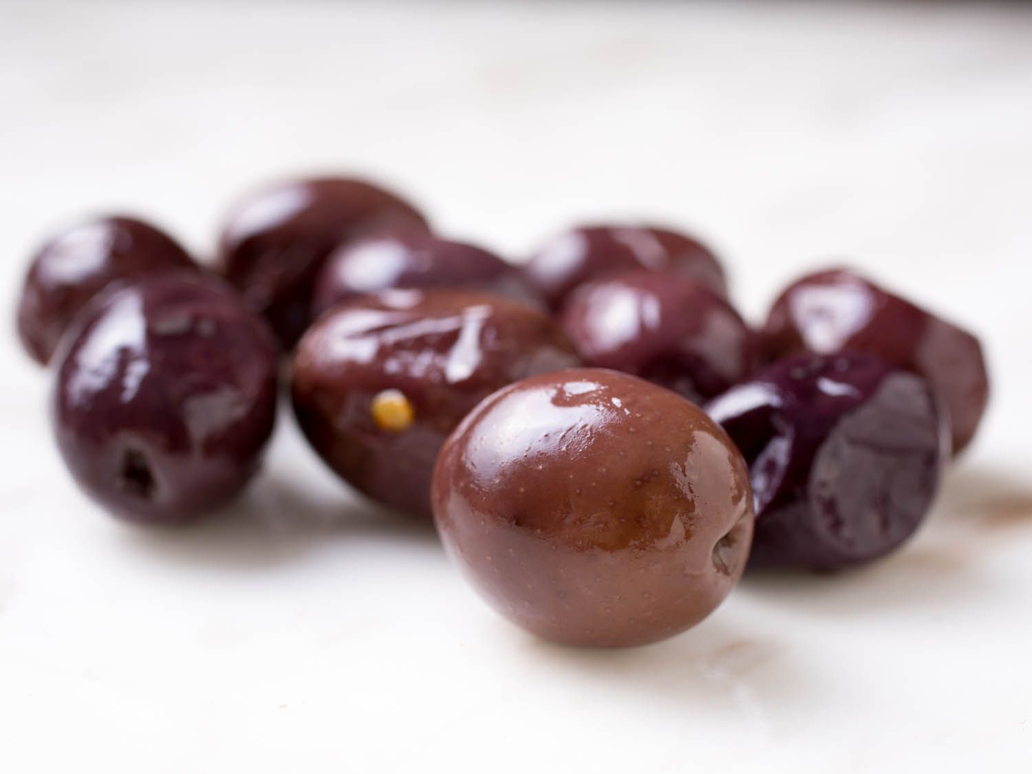 Closeup of shiny, slightly-wrinkled light brown olives on white surface