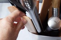 A hand pulling a wooden spoon out of a stainless steel utensil crock