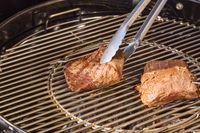 Tongs touching meat on the Weber Performer Deluxe Charcoal Grill 22