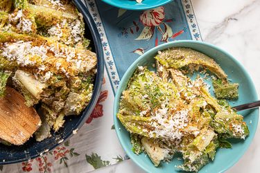 Two servings of a salad featuring greens grated cheese and a wooden spoon