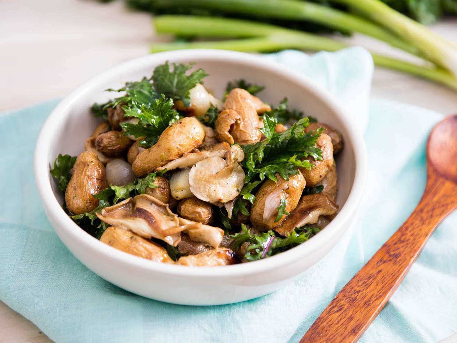 A small white bowl of Roasted Potato and Shallot Salad With Marinated Mushrooms and Kale.