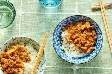 2 bowls of minced pork on white rice in a blue bowl and a white bowl, with chop sticks and glasses of water on a green tablecloth