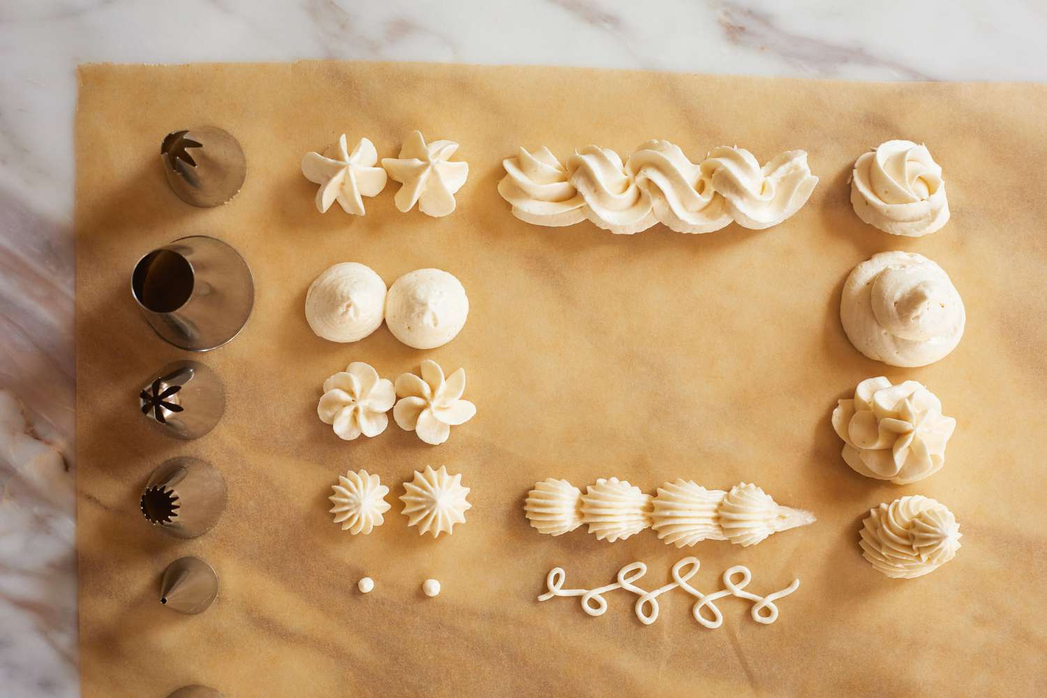 Five piping tips beside five rows of piped frosting on a piece of brown parchment paper