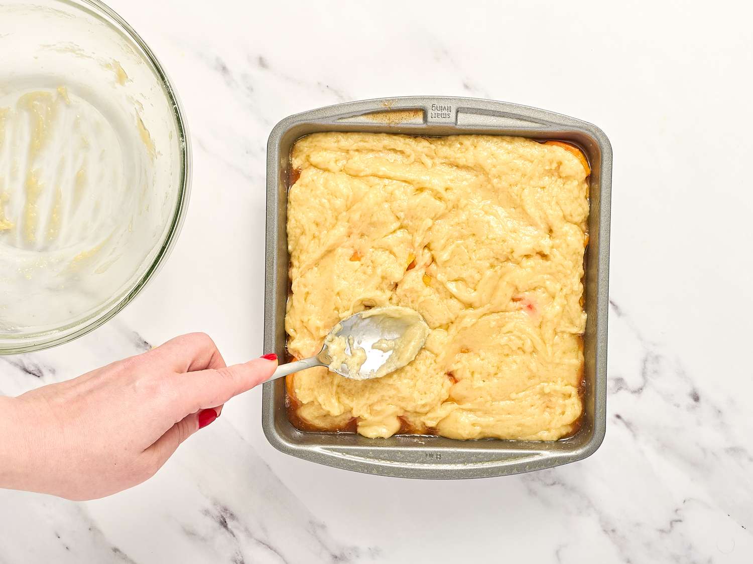 Person spreading batter in a square baking pan with a spoon bowl with remnants of batter on side