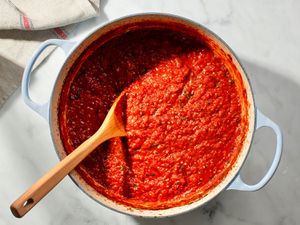 A pot of Italian-American tomato sauce in a dutch oven with a wooden spoon.