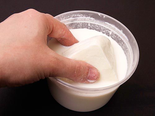 A hand lifting mozzarella out of a container filled with milk.