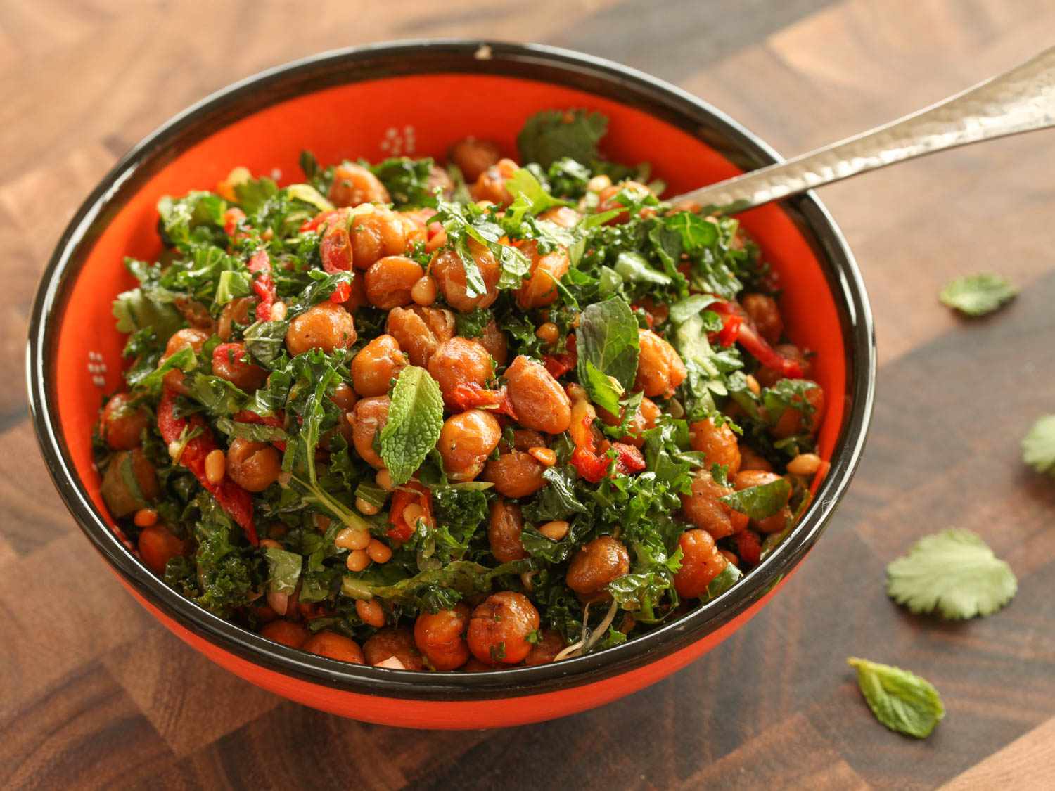 A bowl of roasted chickpea, sun-dried tomato, herb, and kale salad with pine nuts.