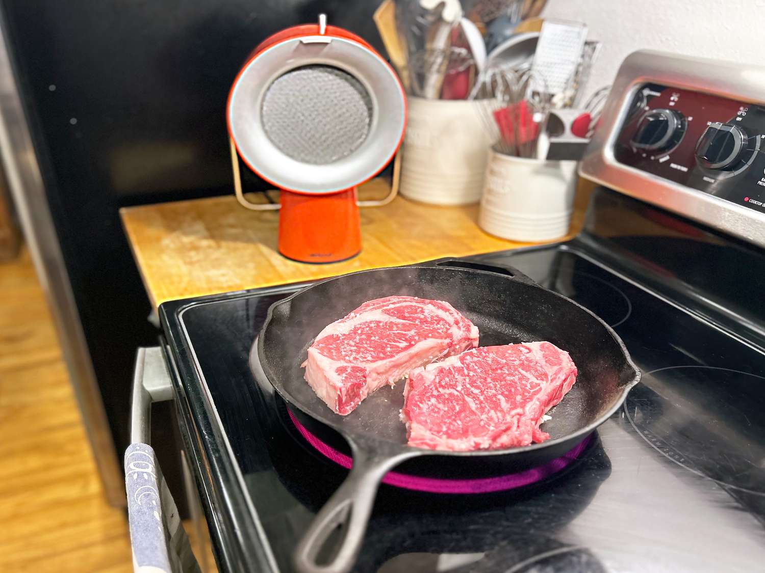 the airhood next to a stove with a cast iron skillet holding two big steaks