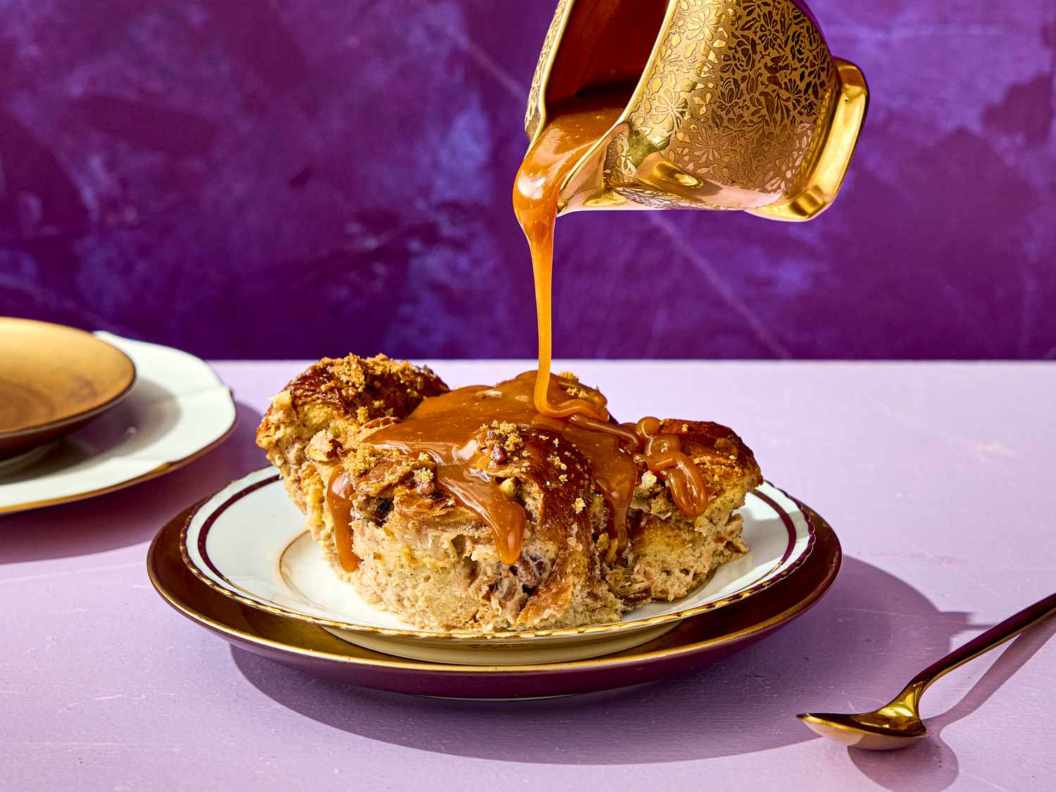 Banana bread pudding on a plate with caramel being poured from a decorative pitcher