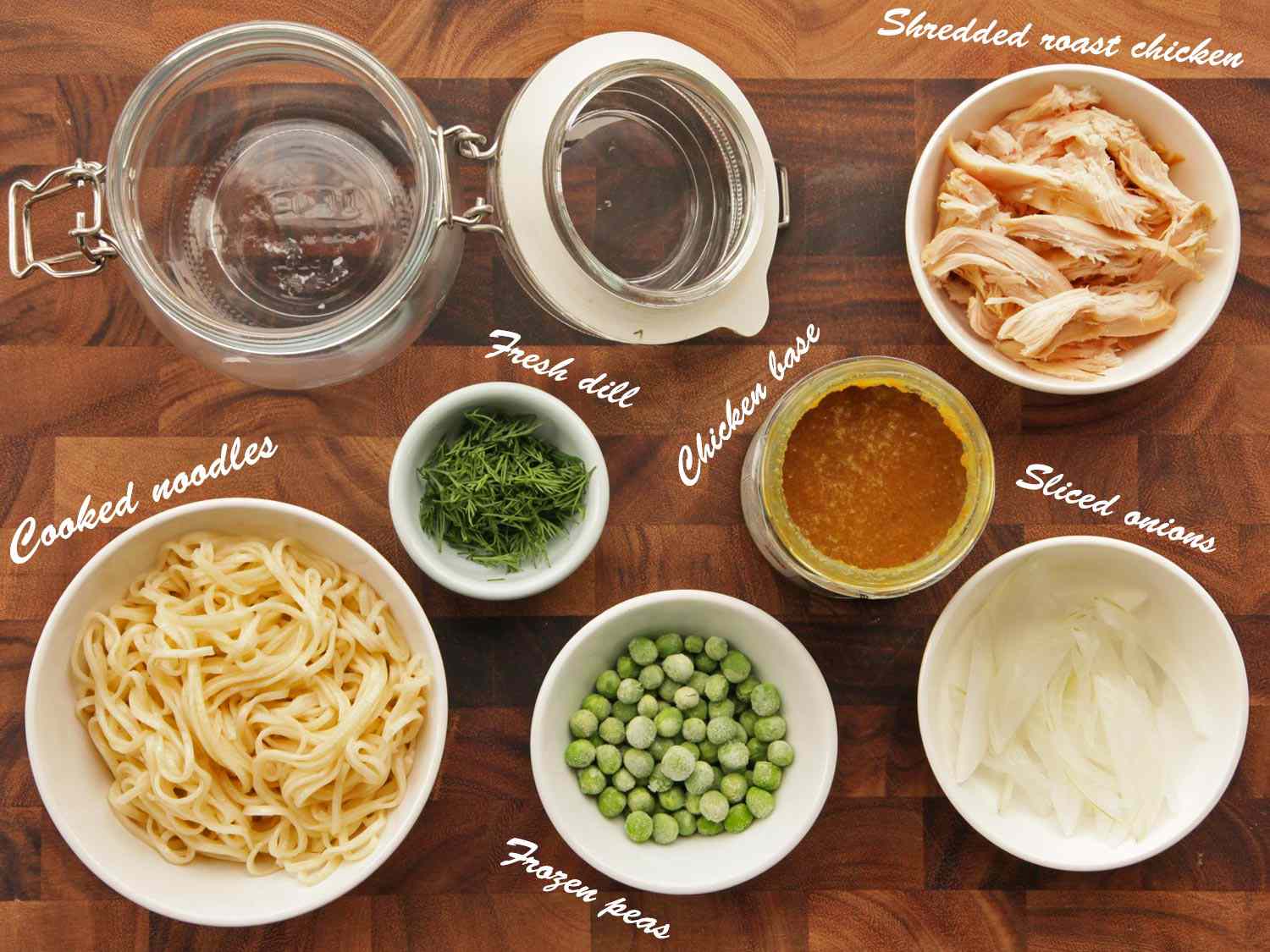 Overhead view of the ingredients needed for chicken and dill flavor instant noodles: shredded roast chicken, sliced onions, chicken base, fresh dill, frozen peas, and cooked noodles.