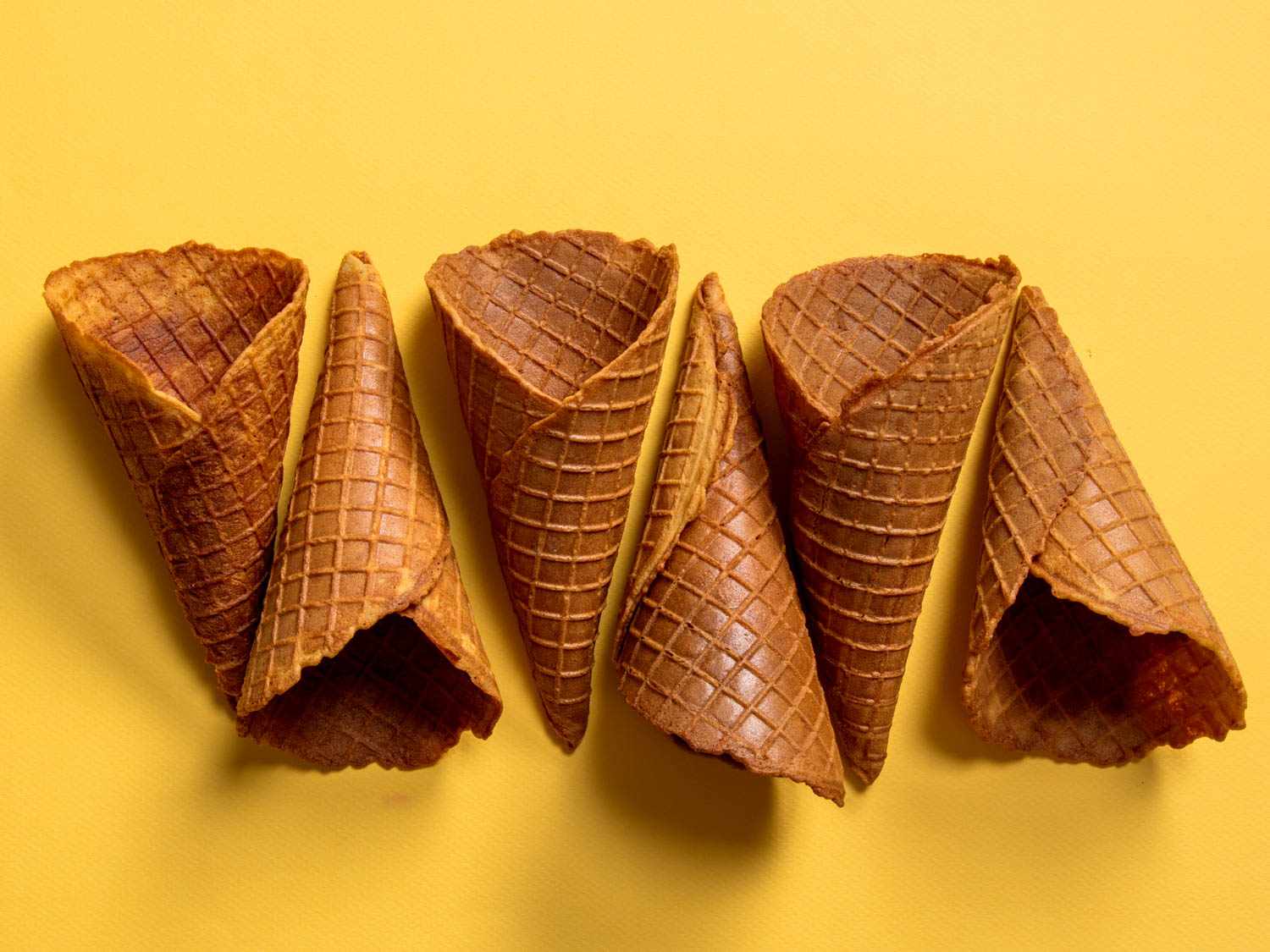 A lineup of golden ice cream cone on a yellow background. 