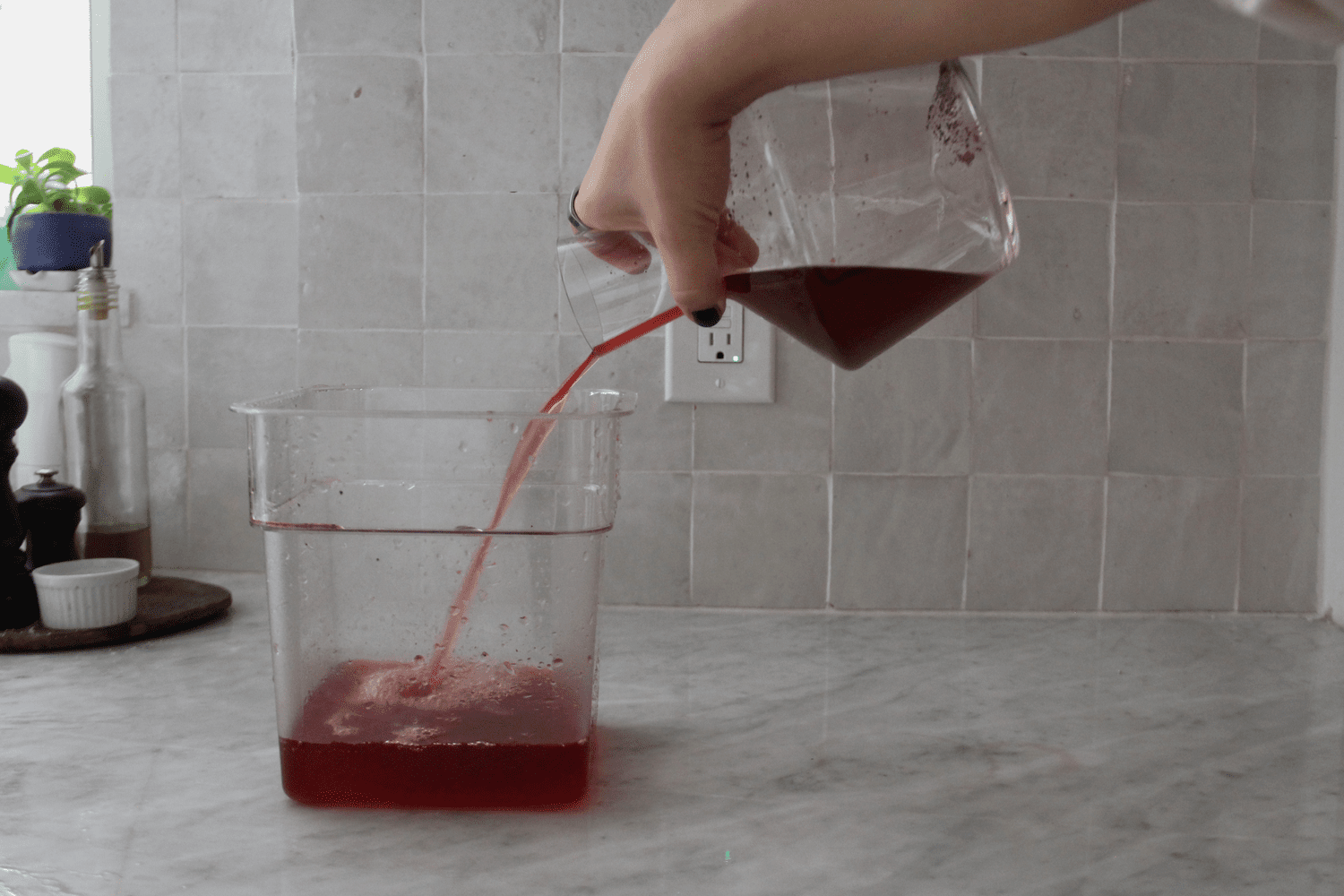 A person holding the short neck of the Zalto wine decanter and pouring into a plastic container