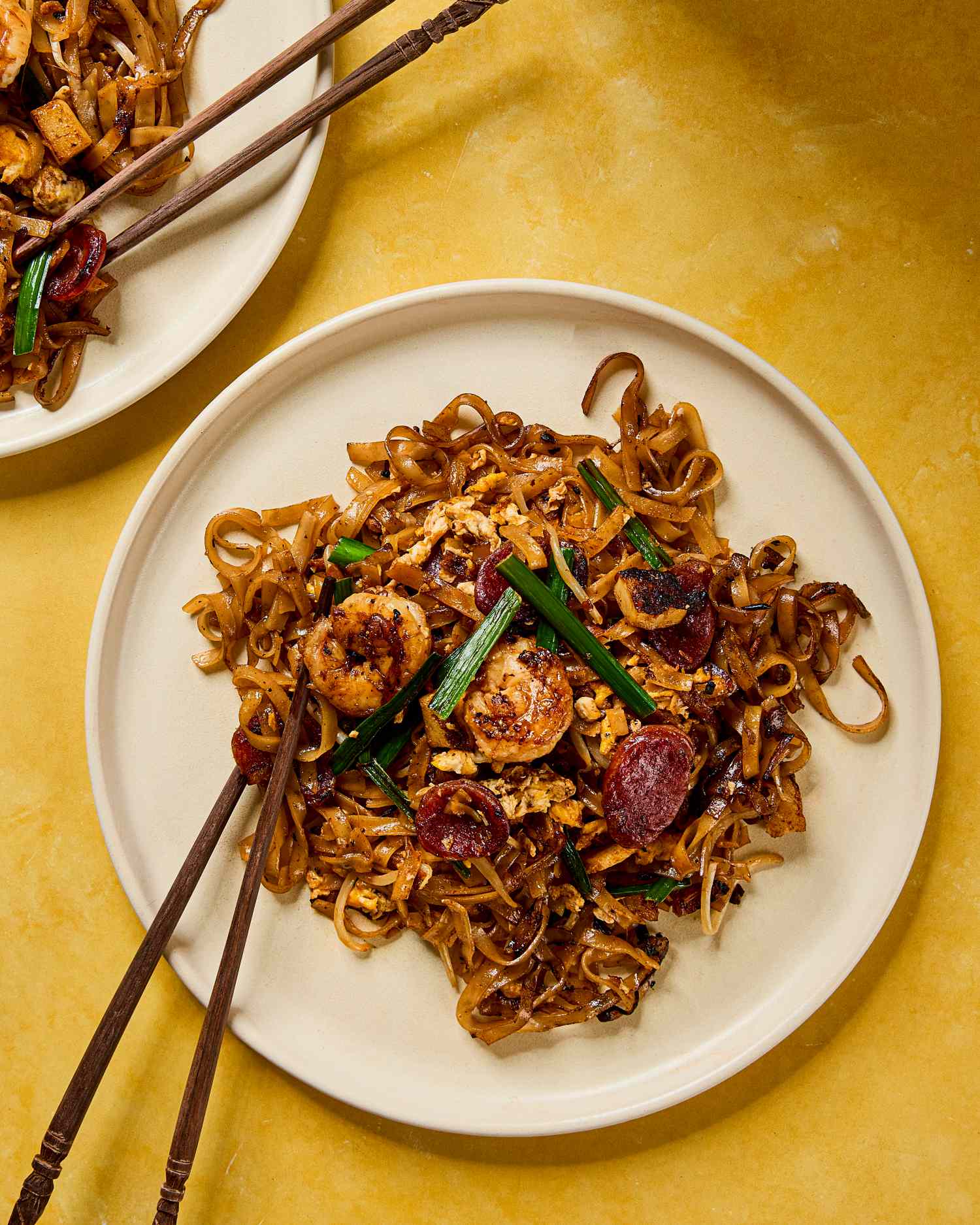 A plate of char kway teow served with chopsticks on a yellow background