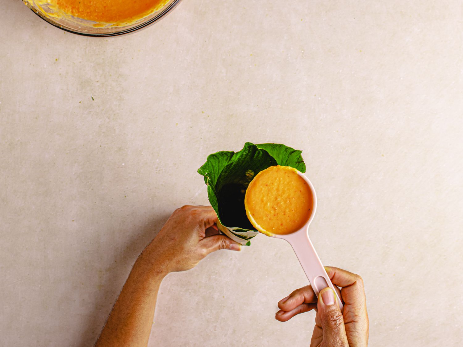 Overhead view of spooning puree into moin moin leaves