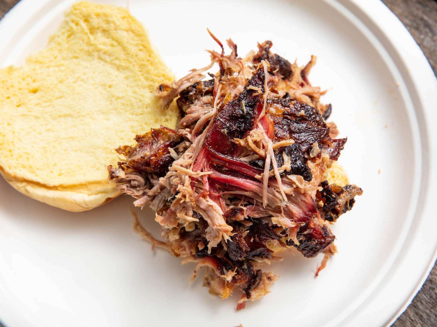 Overhead closeup of the dressed pulled pork piled high on the bottom half of a potato bun.