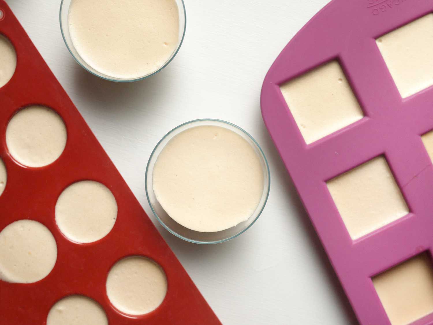 Overhead view of two silicone molds and two glasses filled with the eggnog jello shot mixture, ready to be unmolded.