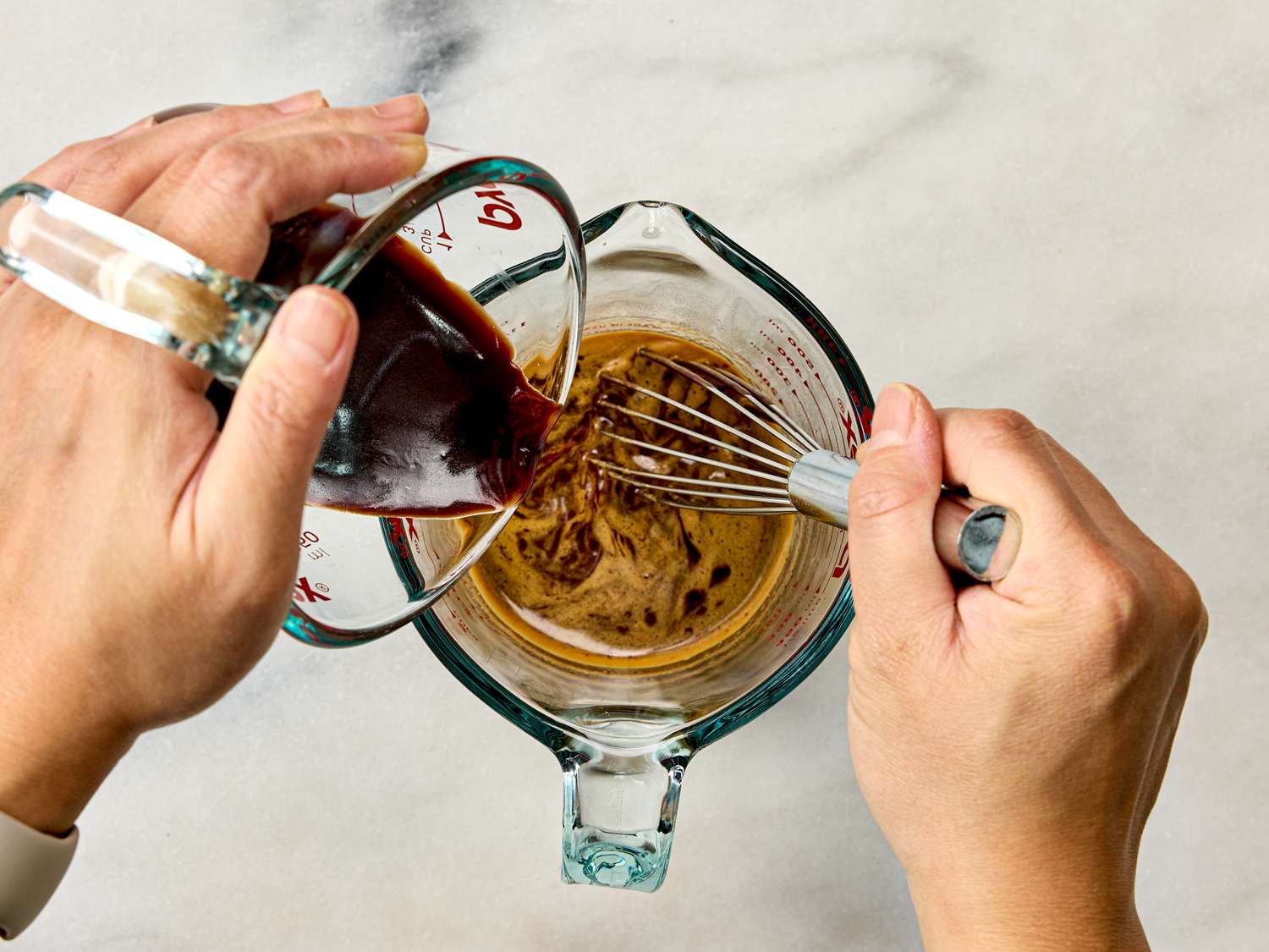 Hands whisking liquid in a glass measuring cup