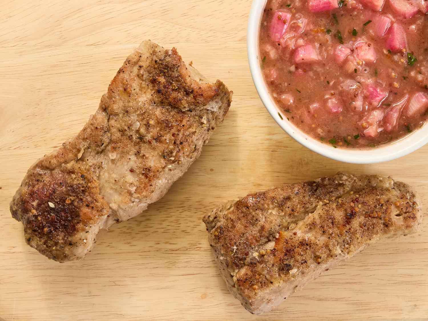 pork tenderloin resting on a wooden board, with rhubarb sauce in a bowl to the side 