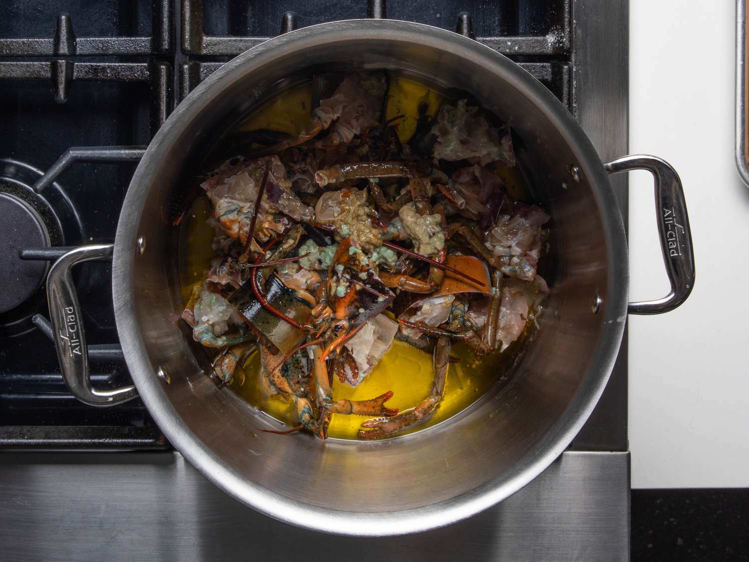 Chopped lobster bodies in a large pool of olive oil in a stockpot: this is the first step in a flavorful and fast lobster stock.