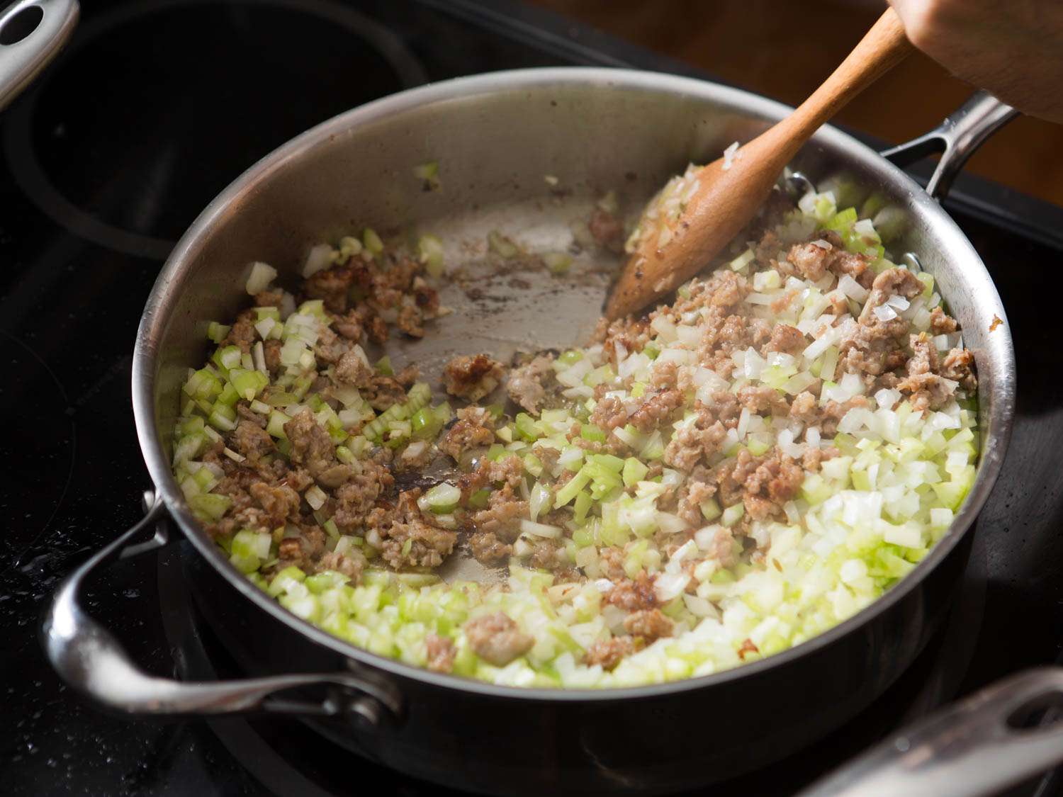 Adding diced onion and celery in a skillet of browned sausage. 