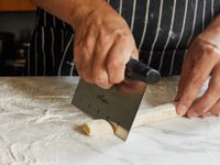A person uses a bench scraper to cut gnochhi