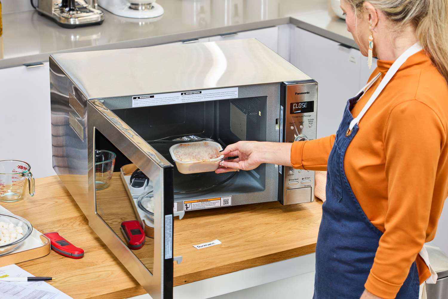 A person putting a microwave meal into the Panasonic - 2.2 Cu. Ft. 1250 Watt SD987SA Full-Size Microwave with Inverter