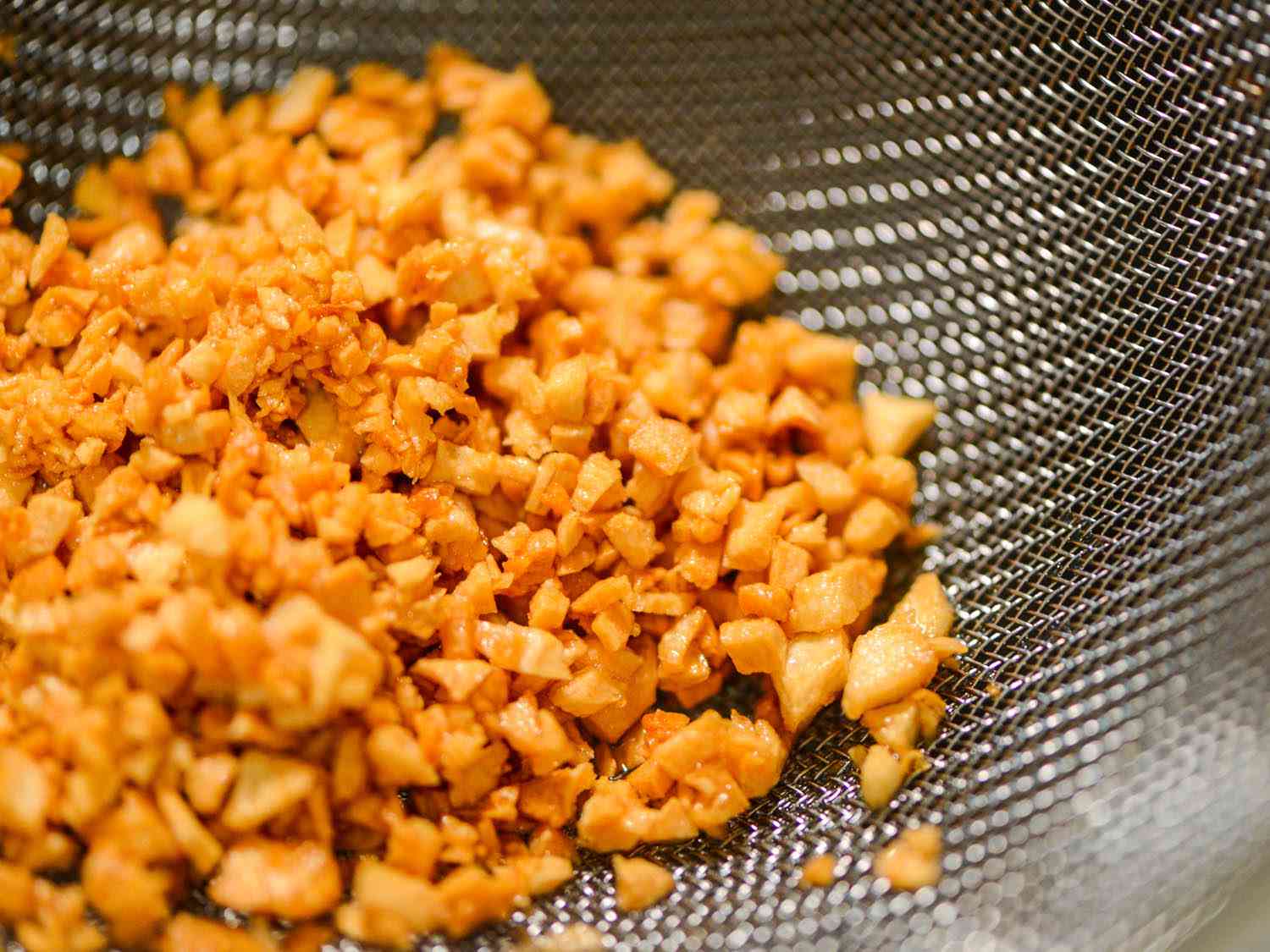 Close-up of golden bits of fried garlic, draining in a fine mesh strainer.