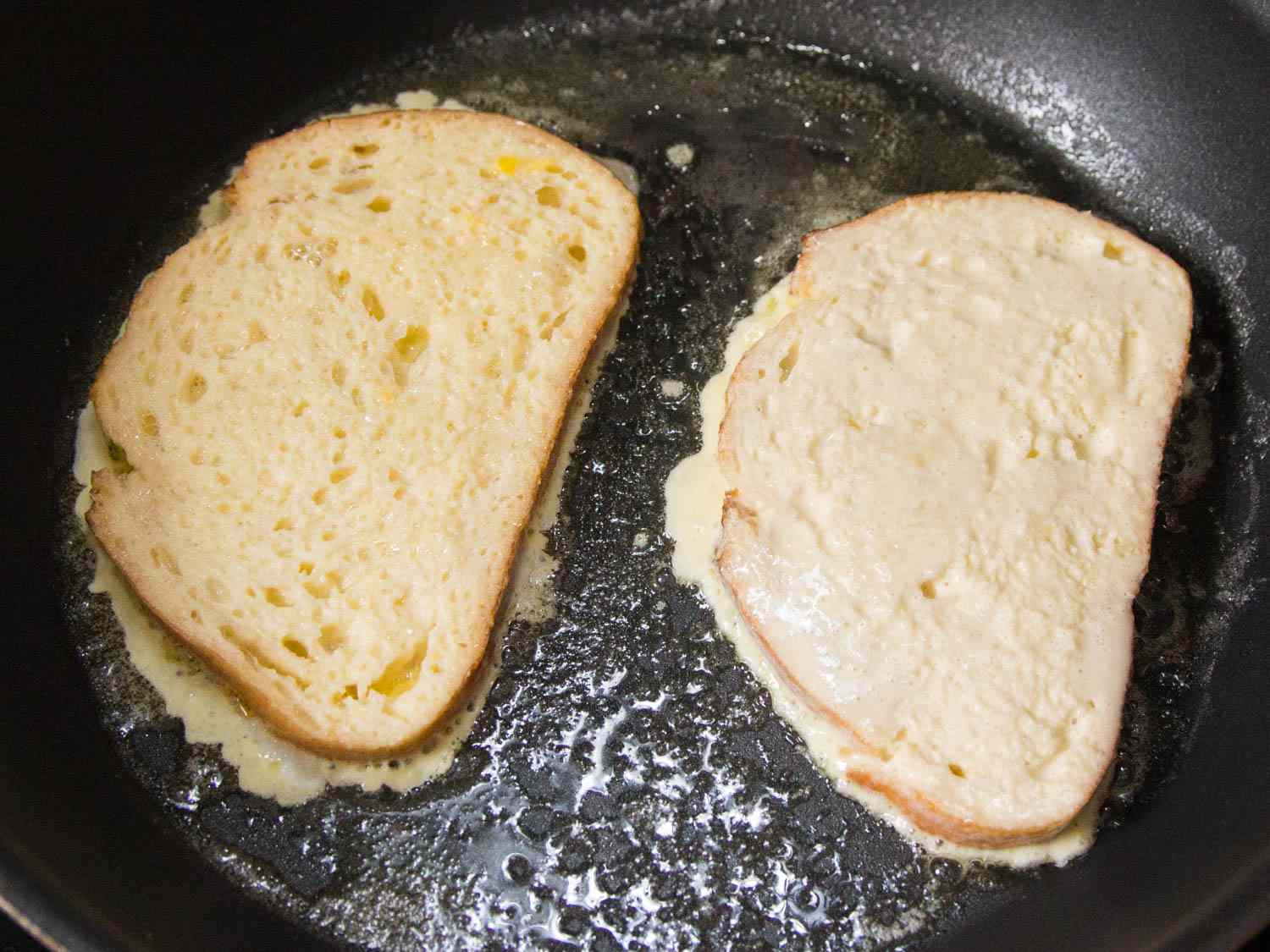 Two slices of custard soaked bread cooking in a skillet.