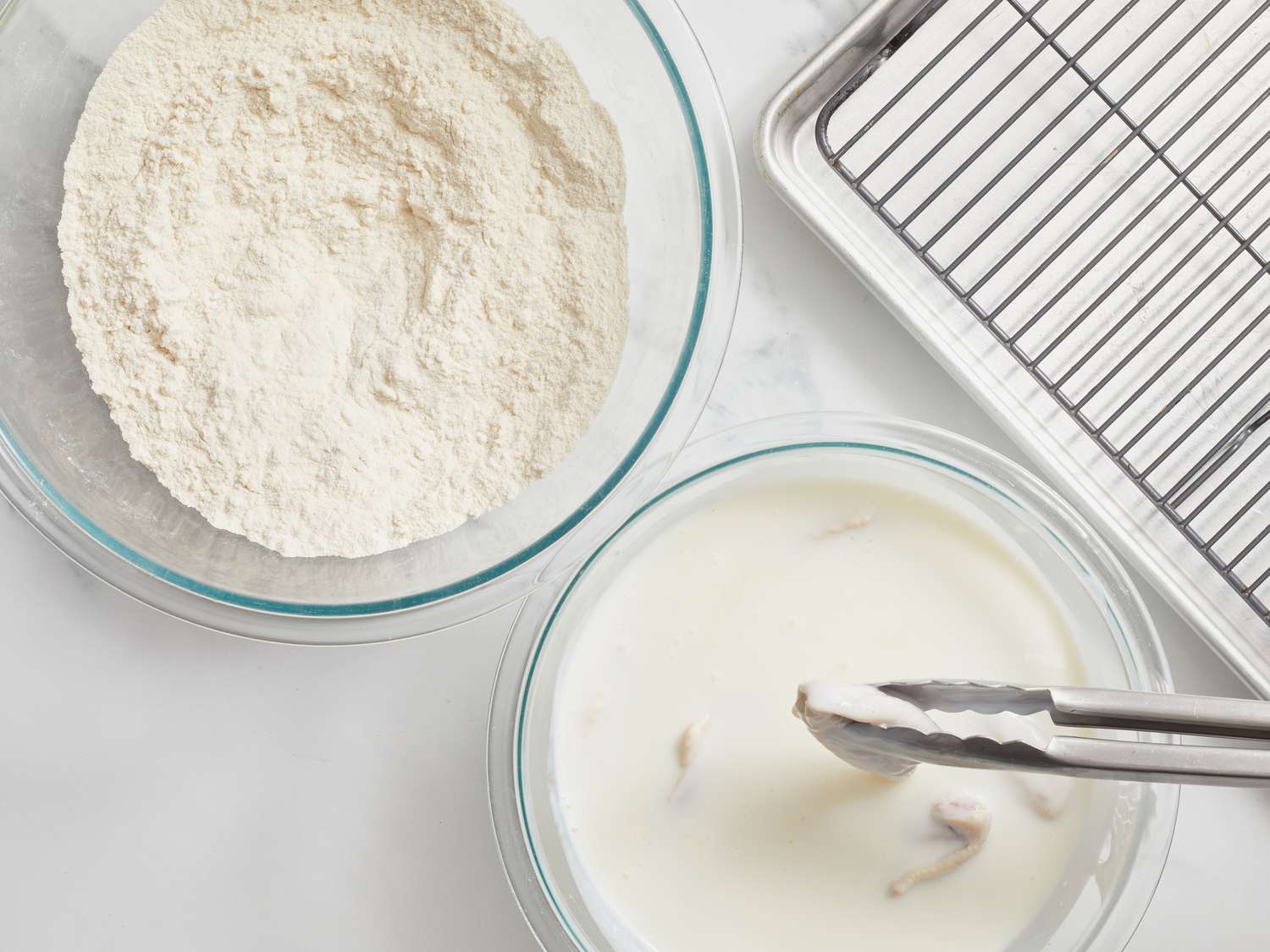 Tongs dipping chicken in buttermilk