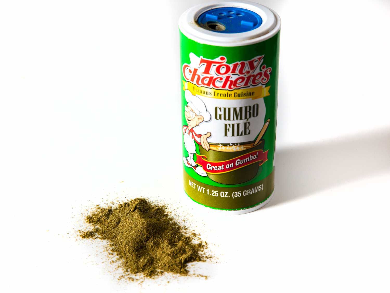 A photo of filé powder in the container, with some sprinkled to show what it looks like: it's a fine powder with a green-brown color.
