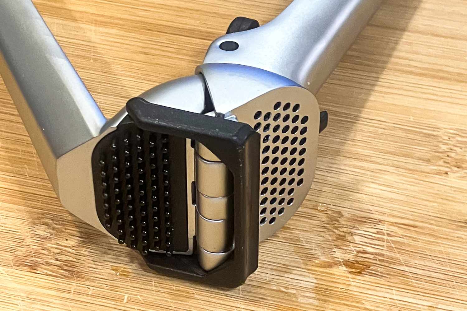 A metal garlic press lying on a wooden surface