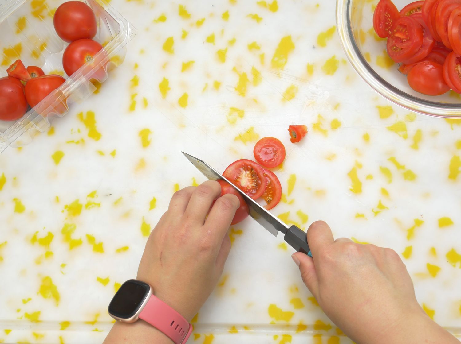 Hands slicing tomatoes on a cutting board a knife in use with tomatoes around in containers and a bowl