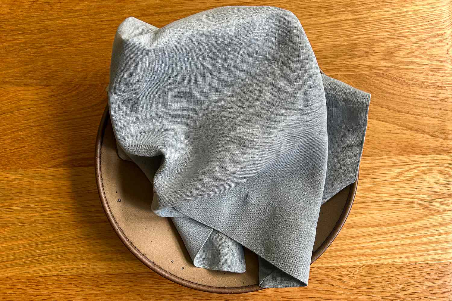 A folded cloth draped over a ceramic dish on a wooden surface