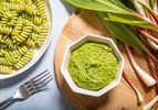 Overhead view of pesto in a small bowl next to ramps and pesto pasta
