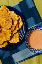 Overhead view of tostones on a blue plate with a blue napkin and bowl of dipping sauce