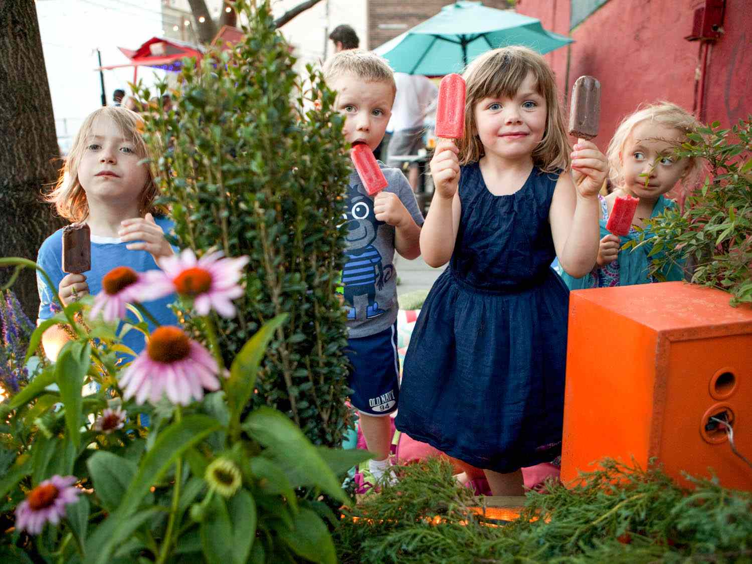 Kids holding popsicles in a garden.