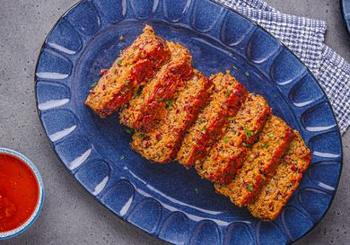 Slices of meatloaf arranged on a serving plate accompanied by a bowl of sauce beside it