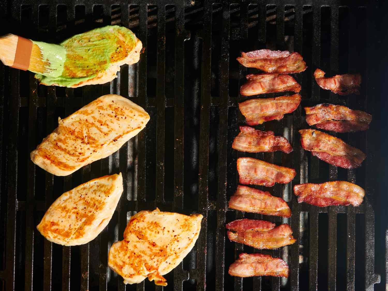 Brushing a coating of green sauce all over the top side of one of the chicken breasts flipped over on the hot side of grill