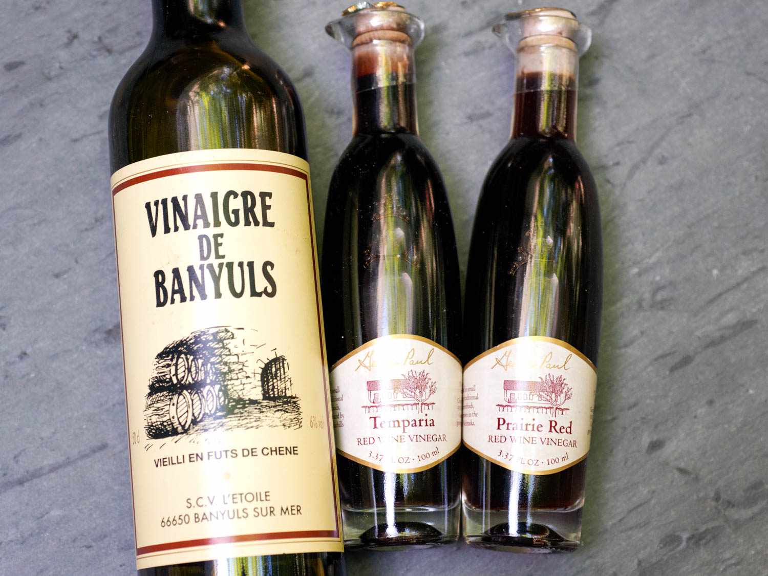 Several bottles of red wine vinegar arrayed on a marble surface.