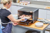 A person placing a rack of raw chicken into the KitchenAid Dual Convection Countertop Oven with Air Fryer