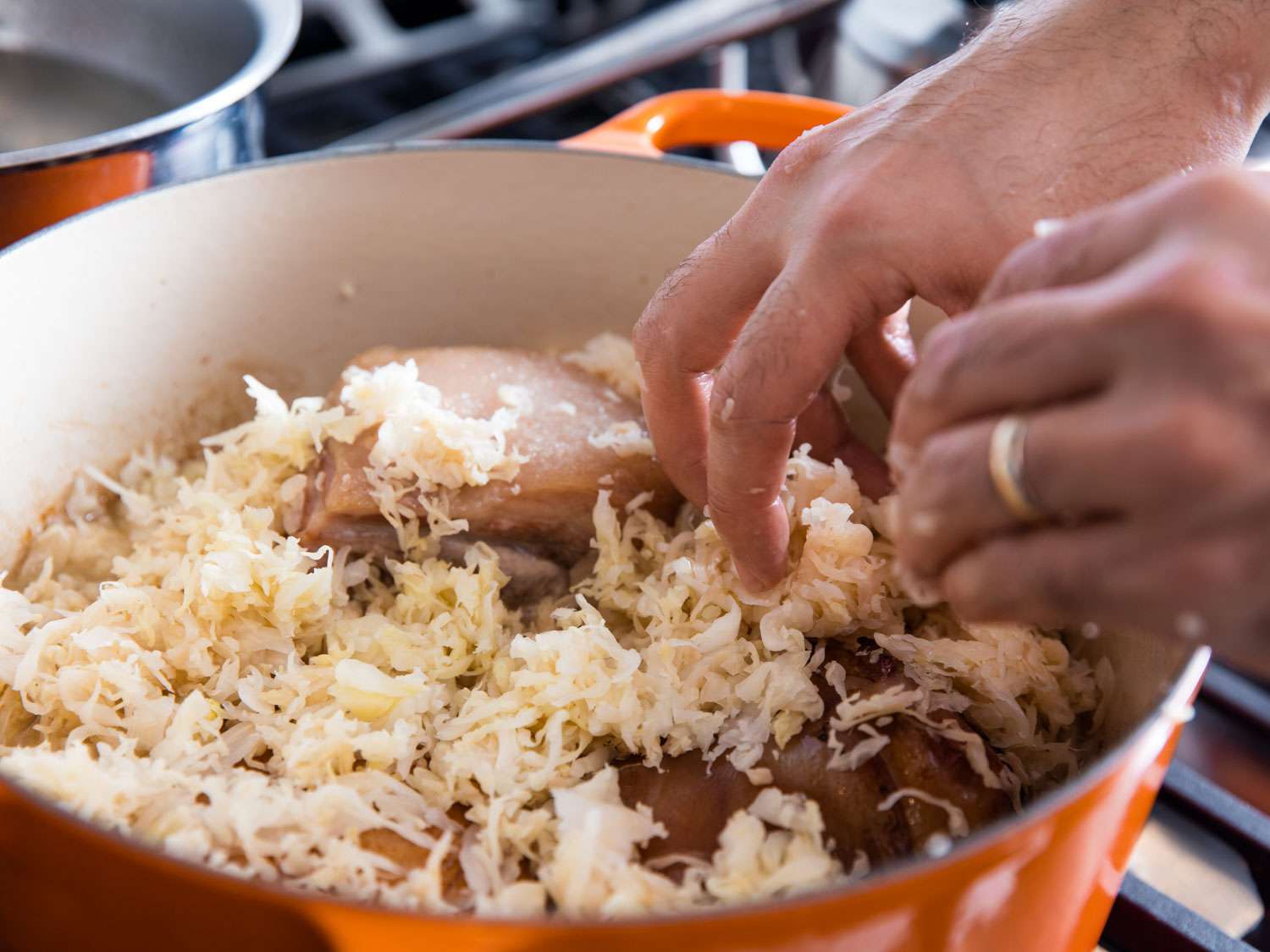 Author adding sauerkraut to the Dutch oven for homemade choucroute garnie.
