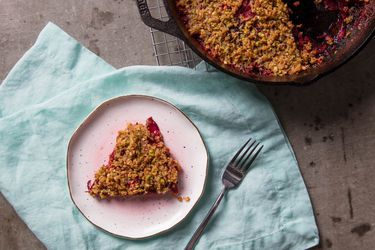 Overhead view of creamy beet gratin with pistachio crumble, served on a small plate. A skillet full of the gratin is nearby.