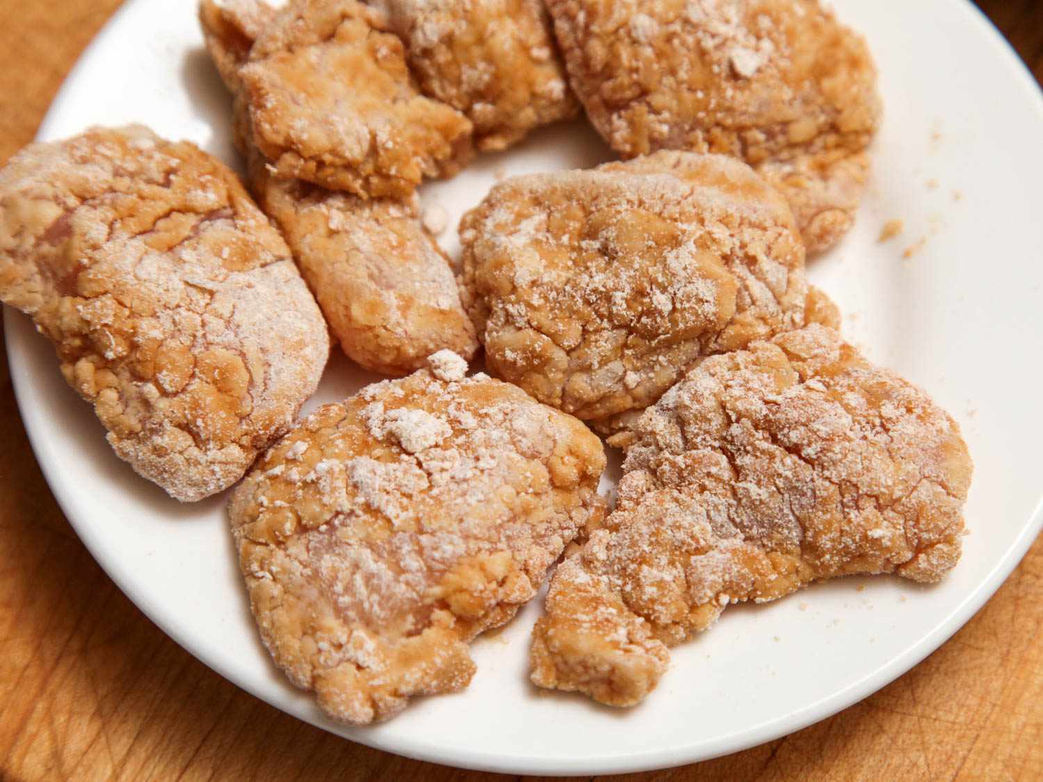 Double-breaded chicken thighs on a white plate before frying for General Tso's chicken.