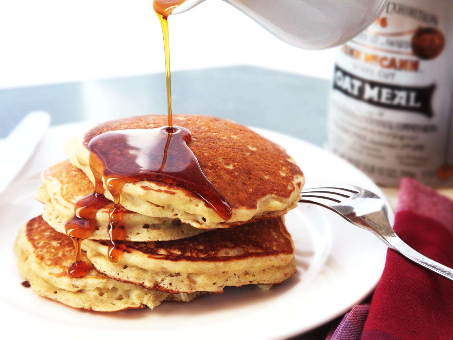 A plated stack of oatmeal and brown butter pancakes with maple syrup being drizzled on.