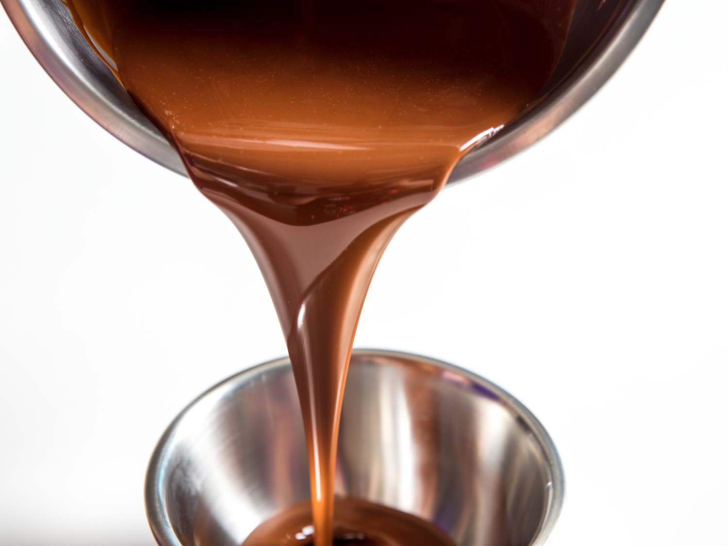 Pouring melted milk chocolate from one bowl to another for dipping Klondike Bars.