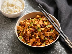 A bowl of spicy mapo tofu with a side of rice.