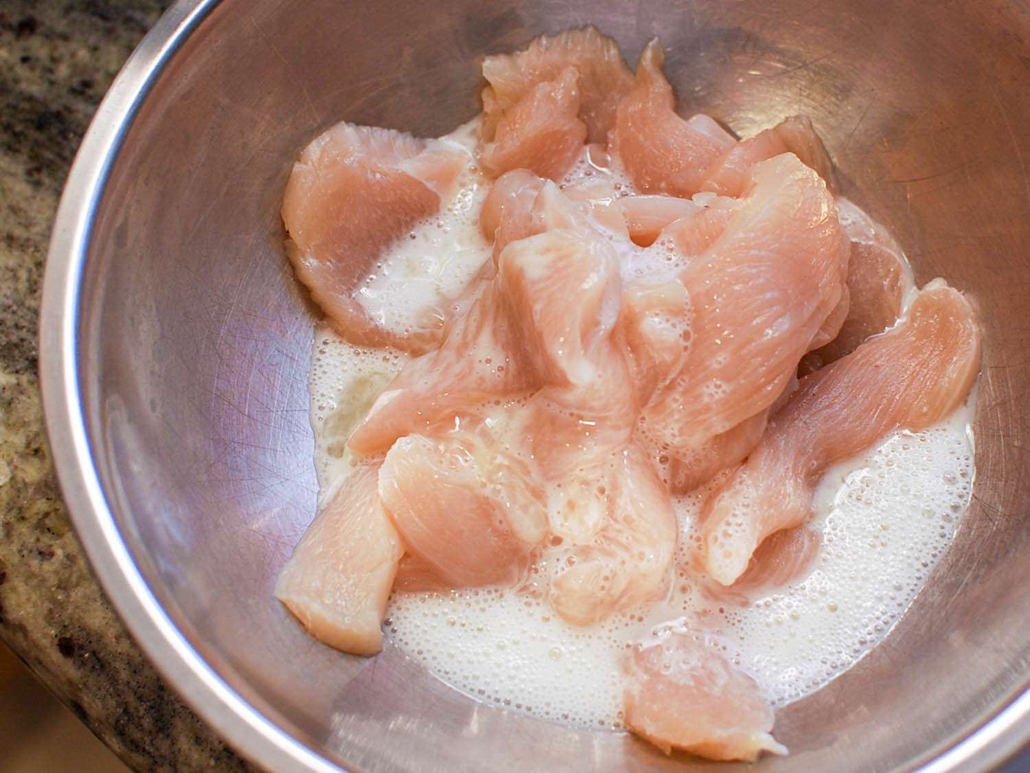 Overhead view of chicken strips marinating in cornstarch-egg white mixture.