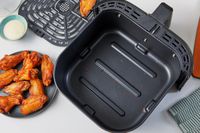 A crumb filled Instant Pot Vortex Plus 6-Quart 6-in-1 Air Fryer basket next to a plate of chicken wings