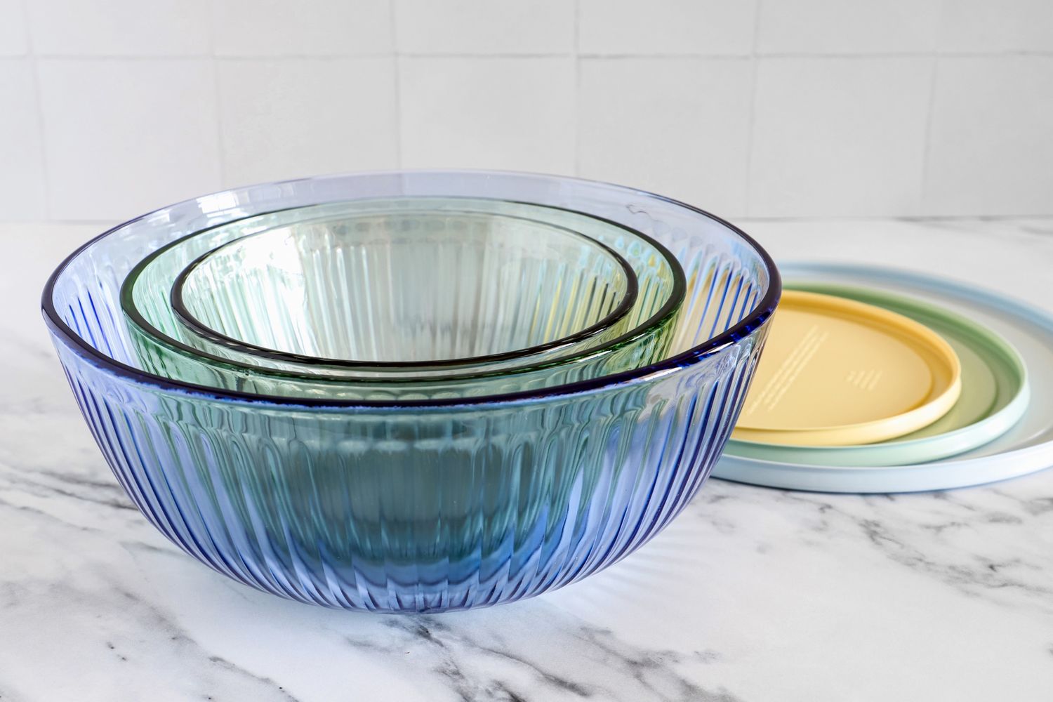 Stacked tinted glass mixing bowls with lids on a marble surface