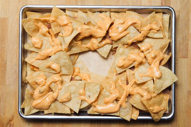 Cheese-sauce covered tortilla chips on a sheet pan for nachos.